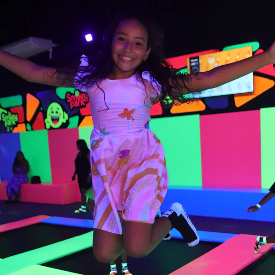 Criança pulando em uma cama elástica neon do Smiley Park