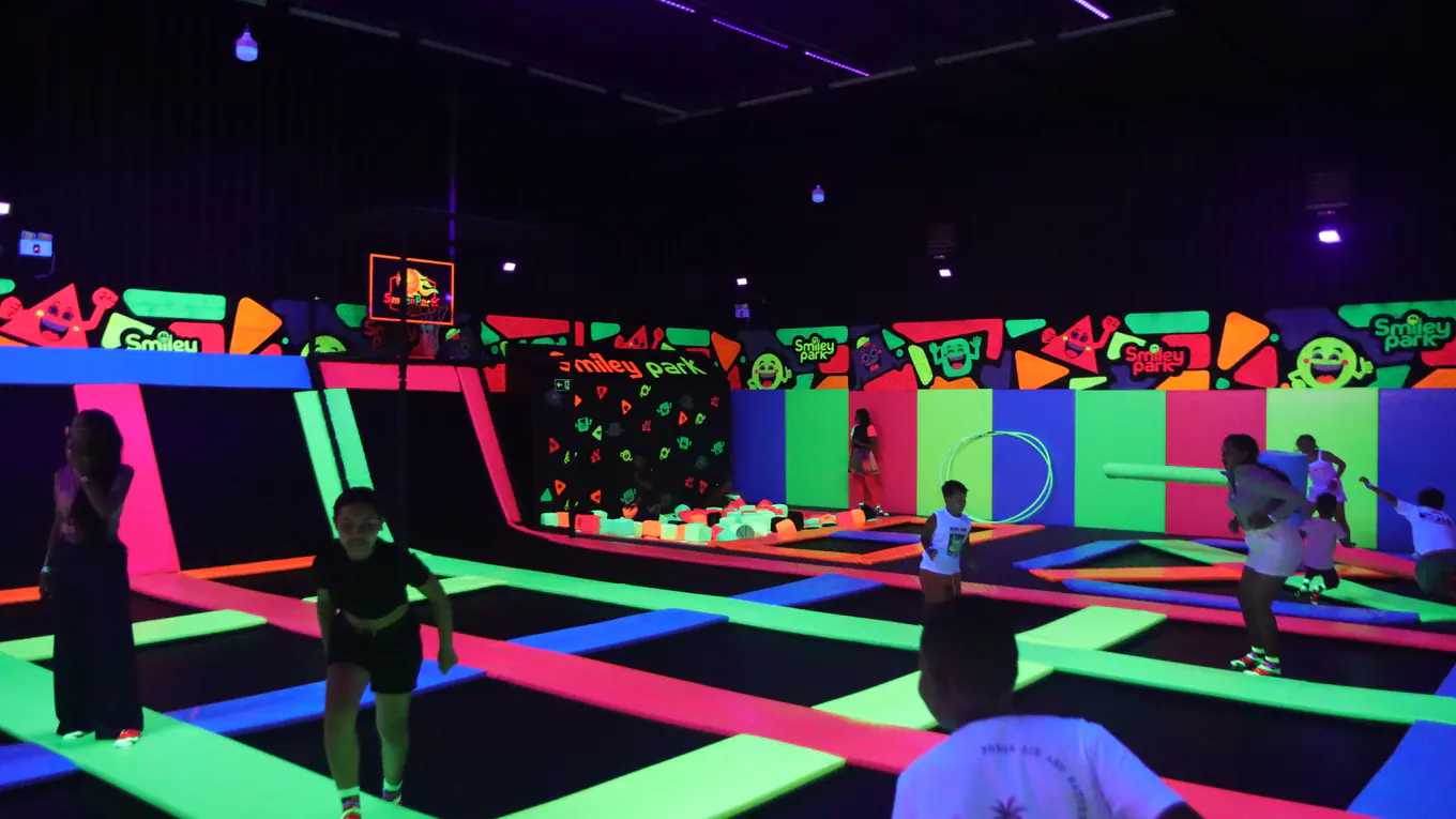 Área de trampolins neon do Smiley Park com crianças se divertindo
